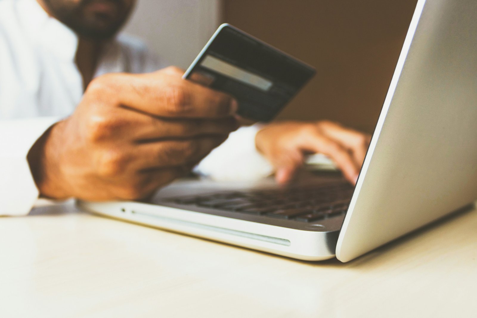 A bank card held in one hand while the other types on a laptop.